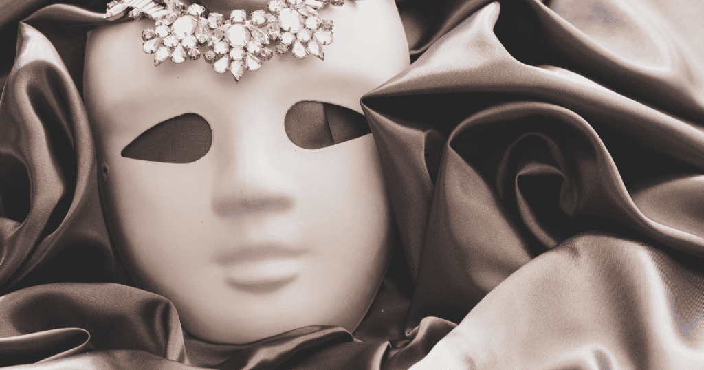 A decorative white mask adorned with jewels rests on smooth satin fabric, representing the kindness mask.