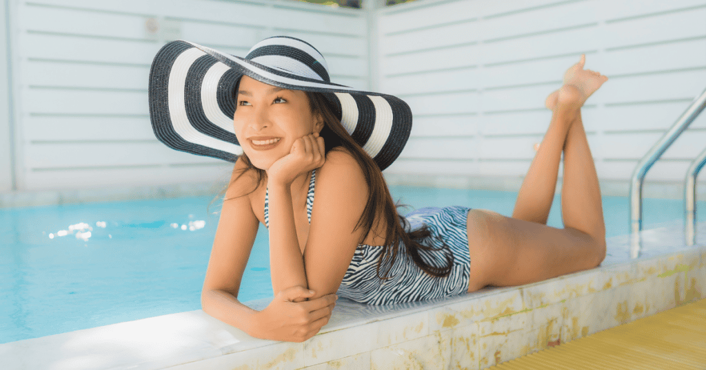 A woman lounges confidently by the pool in a striped swimsuit and wide-brimmed hat, radiating calm and self-assurance — a powerful image of someone who has traded people-pleasing for genuine self-trust.