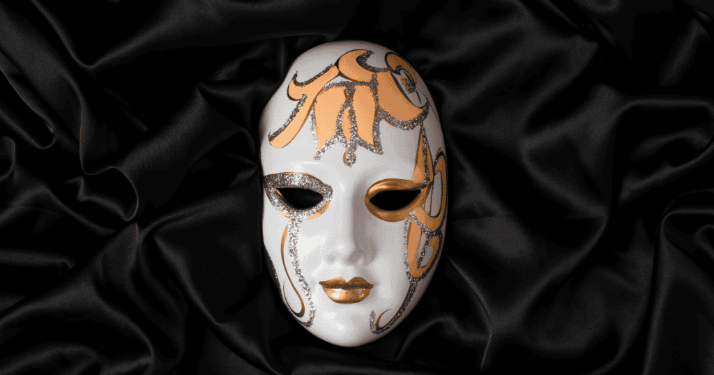 A gold and white ornate masquerade mask with glittering details resting on black satin fabric, symbolizing the rescuer mask.