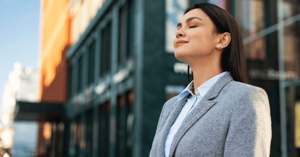 A confident woman stands outdoors with her eyes closed and a calm smile, embodying self-control and emotional strength in the face of conflict.