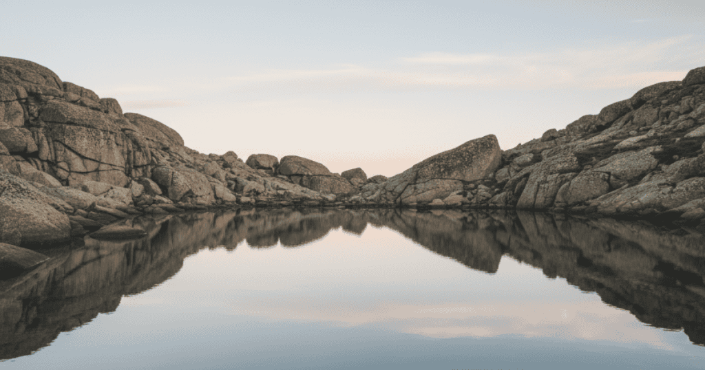 A still lake reflects rugged mountains under a clear sky; this peaceful, unwavering landscape illustrates the inherent power found in quietly maintaining one's personal limits.