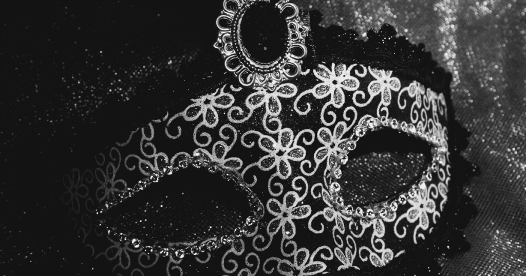 A black and white floral masquerade mask decorated with lace, gems, and an ornate brooch at the top, representing the top-tier mask.