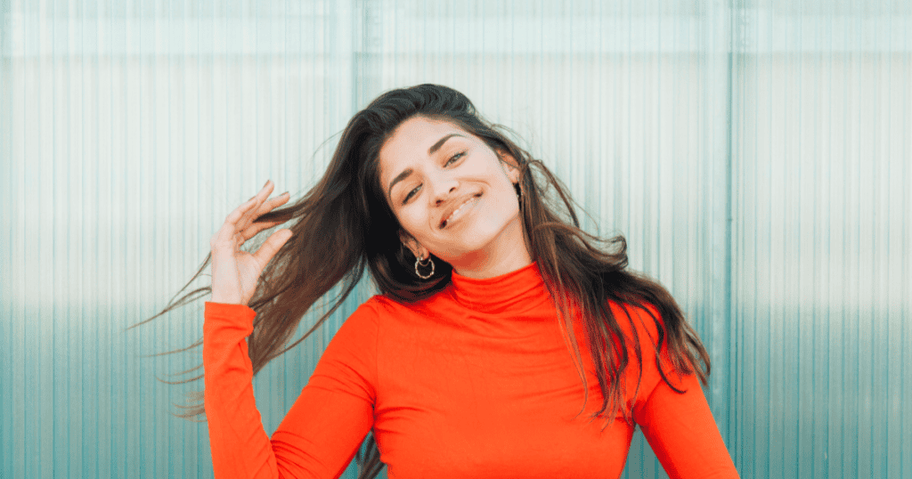 A confident woman in a bright red top smiles while flipping her hair, representing the confidence and freedom that come from mastering the โNoโ boundary.