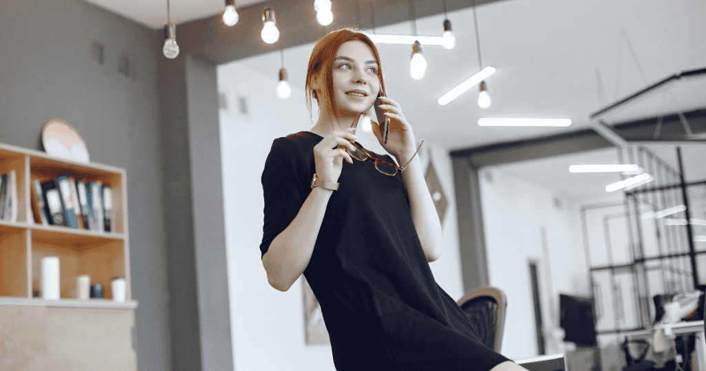 A woman in a black dress stands in an office while talking on a phone, representing an important message being conveyed.