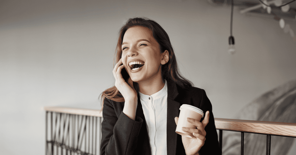 A woman laughs while talking on the phone and holding a coffee cup, symbolizing the confidence and ease that come from strong boundaries against a narcissist.