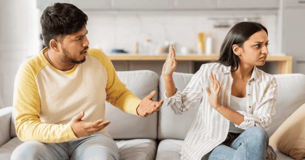A woman raises her hand in frustration while a man argues beside her on the couch to stop a narcissist from arguing.