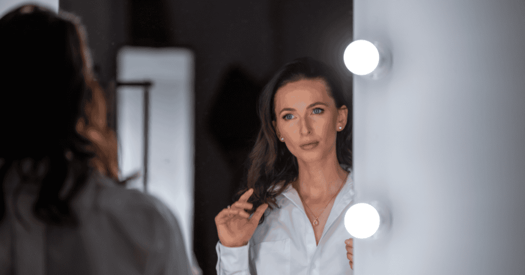 A woman staring at herself in a brightly lit mirror, capturing the self-absorbed “mirror worship” routine common in narcissistic morning habits.