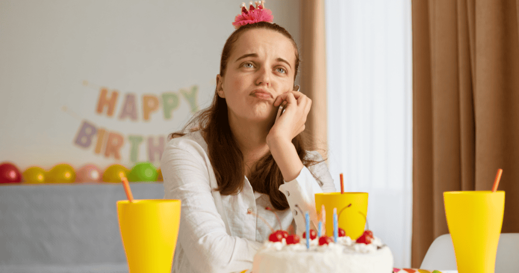 Woman sitting alone at a birthday table with a cake and decorations, looking disappointed, representing how narcissists react when they’re not the center of attention on special occasions.