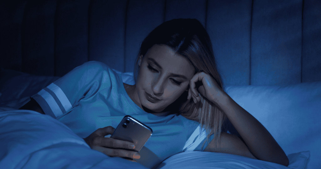 A woman scrolling on her phone in bed late at night, highlighting how narcissists hide secrets and stay glued to their devices before sleep.