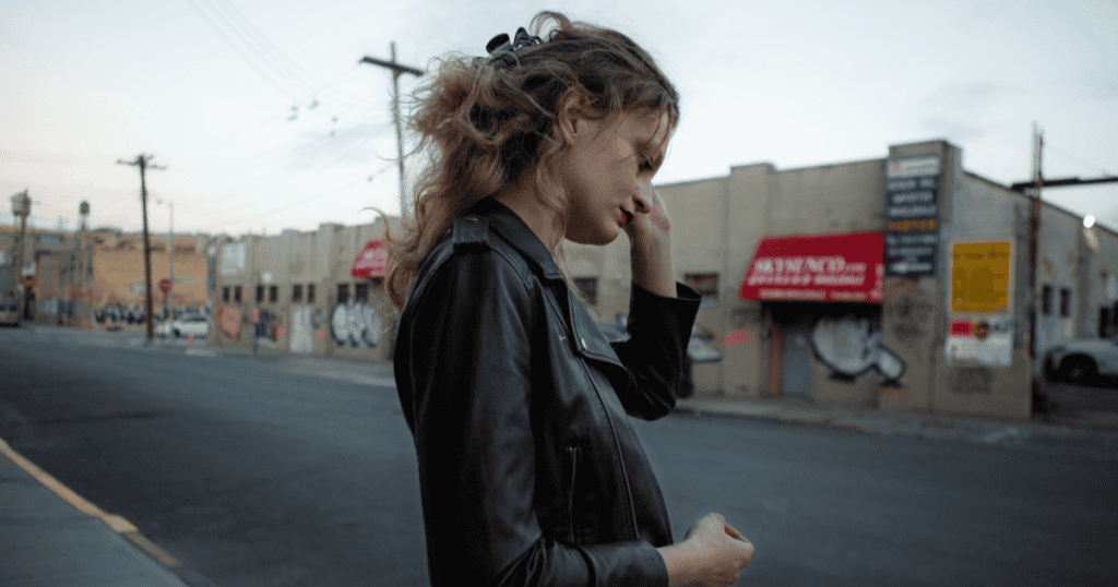 Woman standing on a city street in a leather jacket, looking frustrated and deep in thought, representing how narcissists often create chaos to sabotage others’ moments of success or opportunity.