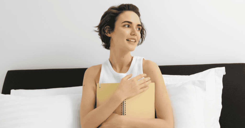A woman sitting in bed holding a notebook, looking conflicted, reflecting how narcissists gaslight you into doubting your own bedtime experiences.