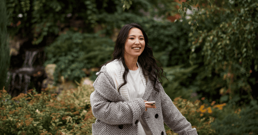 A woman walks through a lush garden with a bright smile, embodying a newfound sense of personal light and autonomy.