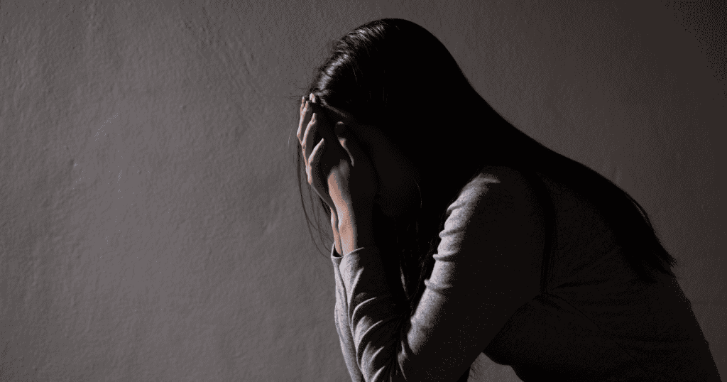 A woman sits in the shadows with her head in her hands, conveying the profound internal pain that stems from a deep betrayal of trust.