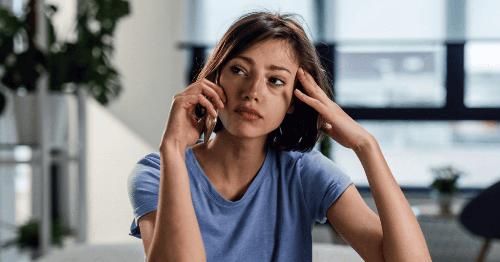 A woman looks upward with a weary expression while holding a phone to her ear, showing the heavy toll of a taxing conversation.