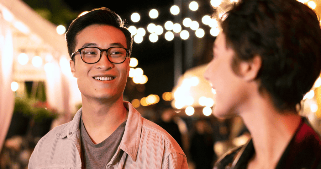 A man smiles warmly at a woman under glowing outdoor lights, illustrating an outward charm that may mask a search for new sources of attention.