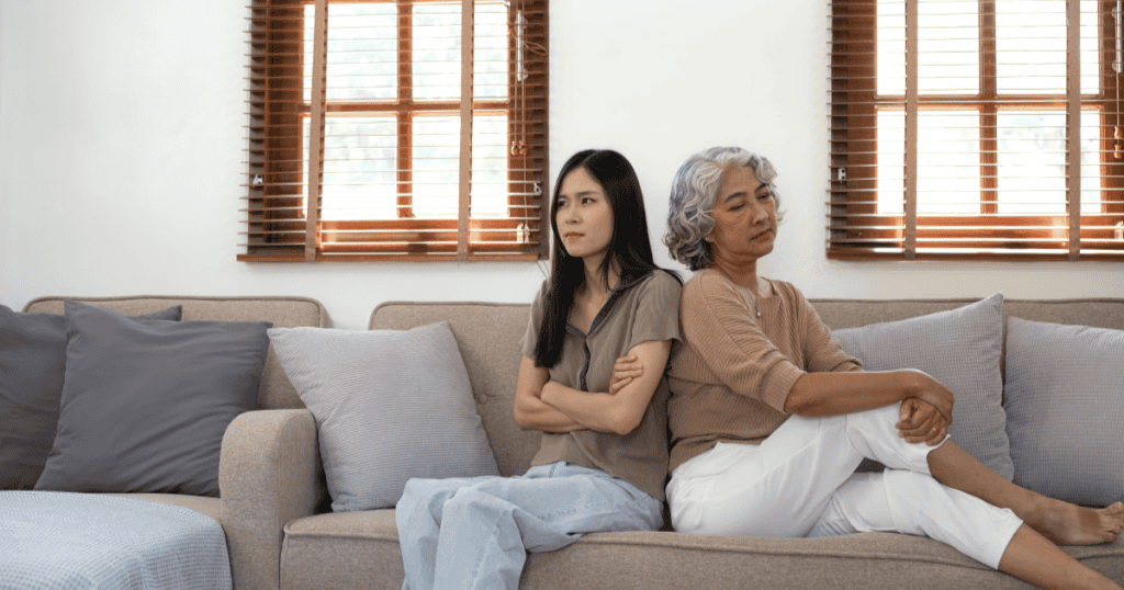 A mother and daughter sit on a couch with crossed arms, capturing the tension narcissists feel when true intimacy inside the home exposes what they work hard to hide.