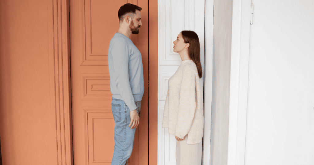 A man and woman stand face-to-face in a doorway, symbolizing how narcissists physically and emotionally block partners from leaving even after the relationship is over.