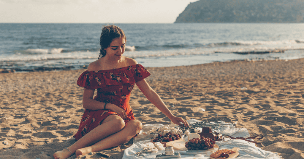 A woman enjoys a peaceful solo picnic on a sandy beach, fully immersed in the moment and unconcerned with the urgency of outside communication.