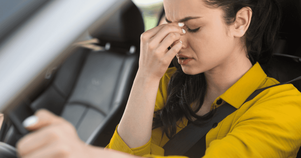 A stressed woman sits in her car gripping the bridge of her nose, overwhelmed by the isolating realization that her emotional needs are being met with a cold indifference.
