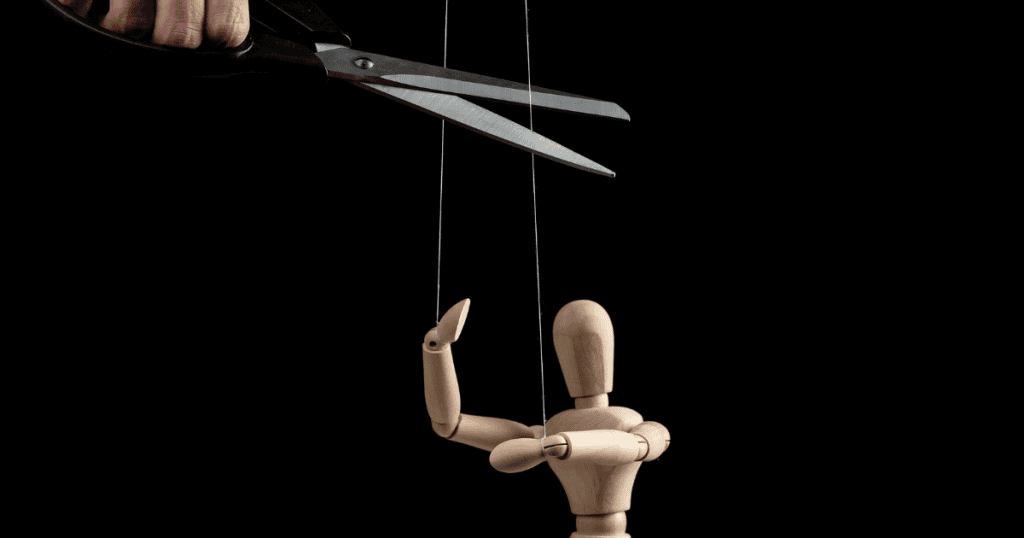A wooden mannequin being manipulated by strings under a pair of scissors, illustrating the moment a controlling influence is finally severed.