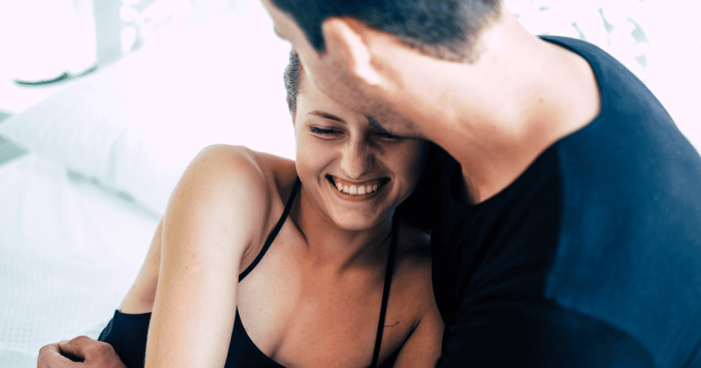 A man leaning in toward a laughing woman in bed, suggesting a connection that may prioritize the physical over the personal.
