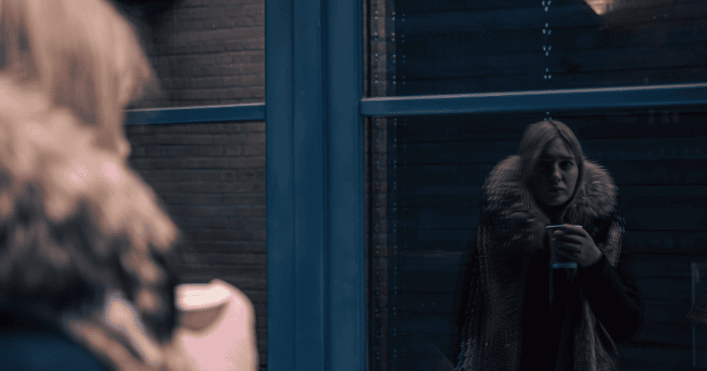 A woman stares blankly at her own reflection in a dark window, illustrating a sense of confinement within one's own environment.