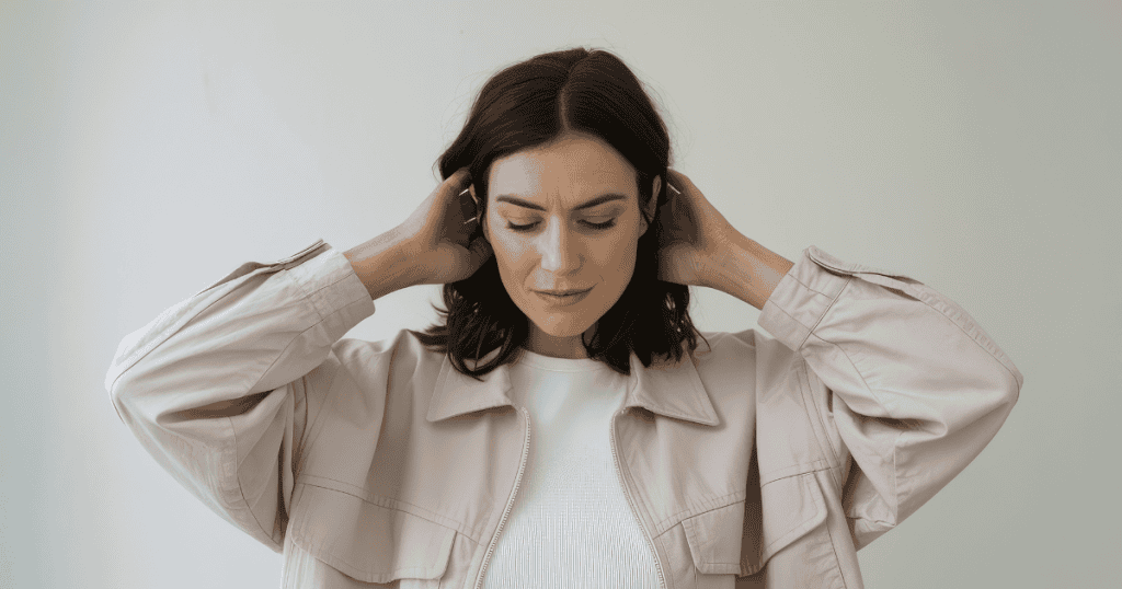 A woman closes her eyes with hands behind her head in a moment of stillness, illustrating the conscious choice to tune out false narratives and center on your own truth.