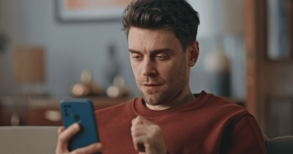 A man intensely focused on his phone while sitting alone, hinting at secretive, obsessive hobbies narcissists hide to protect their carefully crafted image.
