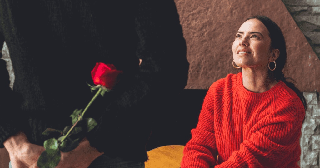 A man hides a red rose behind his back while a woman smiles, demonstrating the kind of thoughtful gesture that signals a healthy dynamic.