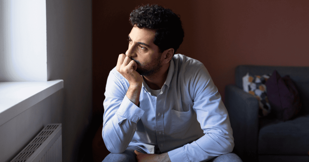 A man sits by a window with his chin resting on his hand, his distant gaze reflecting the depths of a private and guarded interior world.