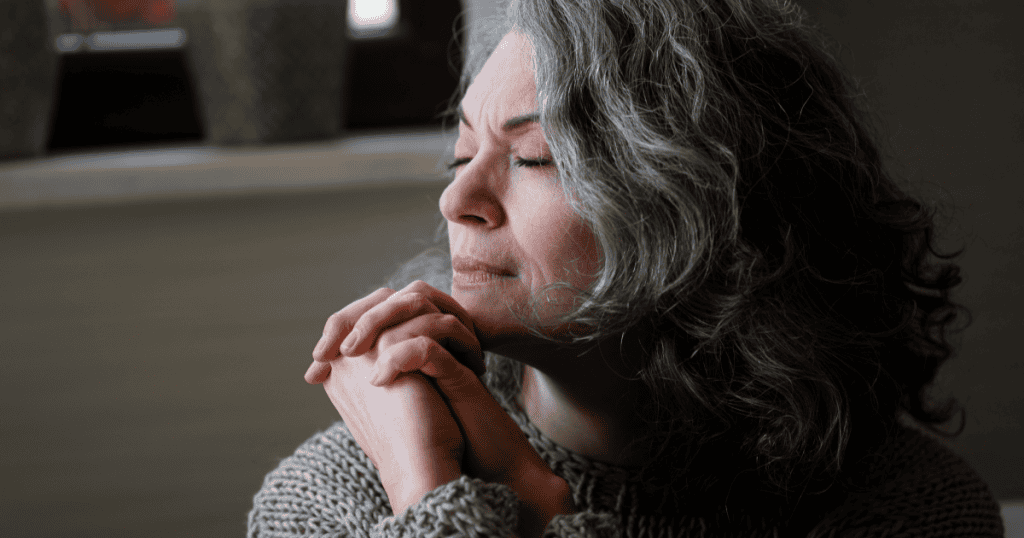 An older woman with gray hair sits with her eyes closed and hands clasped in a serene, prayer-like pose, projecting a false image of innocence that masks her refusal to take accountability for the emotional damage caused to her daughter.
