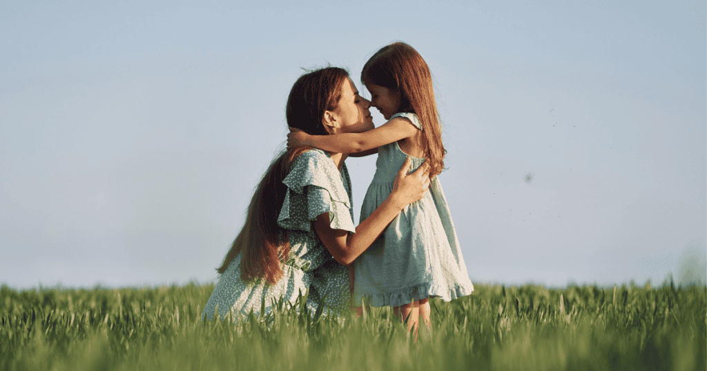A mother and young daughter embrace in a sunlit field, touching noses in a gesture of the nurturing care every child deserves.