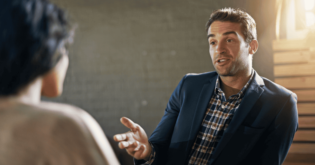 A man in a blazer leans forward with an open gesture, looking as if he is finally ready to articulate the blunt and unfiltered reasons behind his hostility.