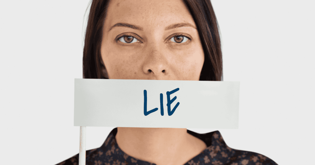 A woman holds a small sign reading "LIE" over her mouth, masking her true identity behind a curated deception.