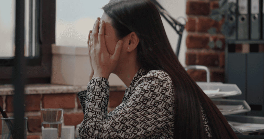 A woman sits at her desk covering her face with her hands, showing the regret and emotional exhaustion that often set in after going back to a narcissist.