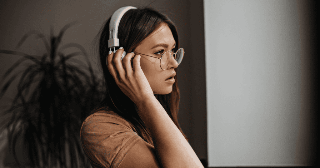 A woman wearing headphones looks off to the side with a focused expression, appearing to tune out the world while waiting for a sound that may not arrive.
