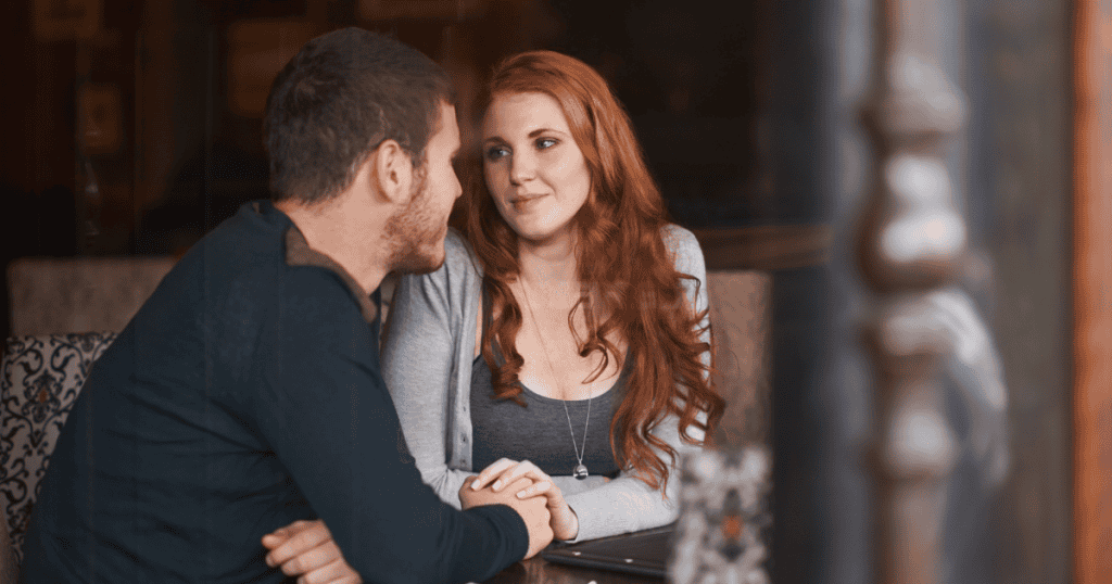 A man and woman holding hands across a table while maintaining intense eye contact, depicting a moment of focus that may carry a hidden agenda.