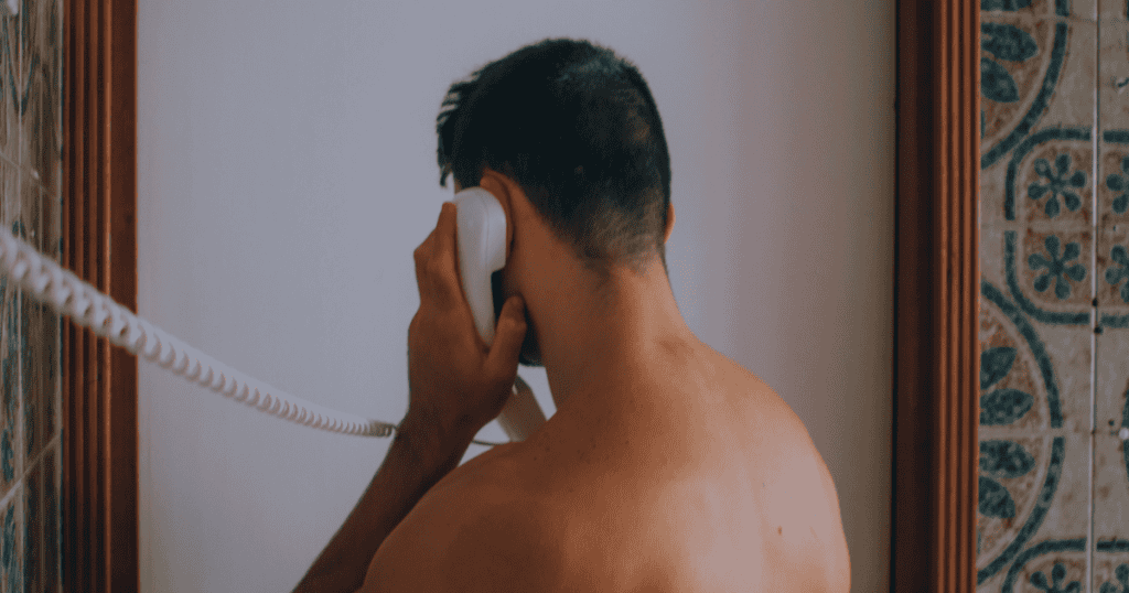 A shirtless man stands with his back to the camera while gripping a telephone receiver, his posture suggesting a desperate attempt to maintain a connection.