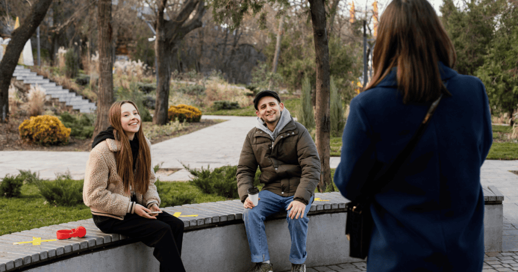 A woman stands still watching her siblings in the park, marking the specific moment clarity arrives and the scene is viewed with new eyes.