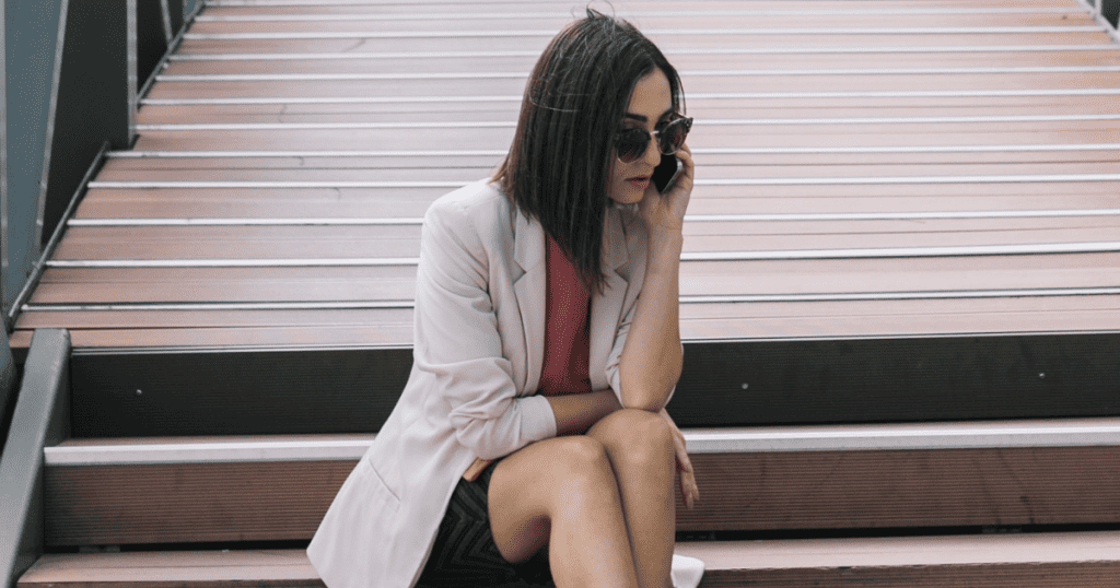 A woman sits alone on outdoor steps engaged in a serious phone call, hinting at the solitary emotional toll and unseen sacrifices that often go unnoticed by others.