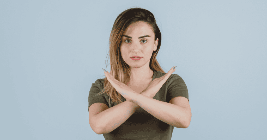 A woman stands with her arms crossed in a firm "X" gesture against her chest; her unyielding posture hints at a deeper, more calculated habit of rejection.