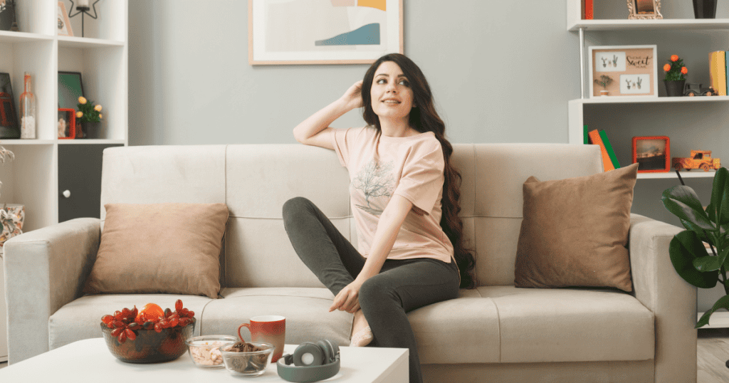 A young woman sits relaxed on a neutral-toned sofa, appearing unburdened as if she has just stepped away from a complex obligation.