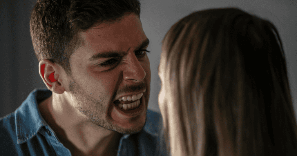A man with a strained, aggressive facial expression shouts closely at a woman, using his intense emotional volatility as a primary point of leverage.