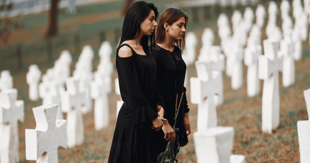 Two women dressed in black stand solemnly among grave markers at a funeral, reflecting how moments of grief can be exploited by narcissists to create tension, control, or quiet retaliation.