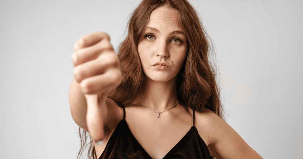A young woman gives a thumbs-down gesture with a calm and detached expression, illustrating the moment of understanding that the negativity originates elsewhere.