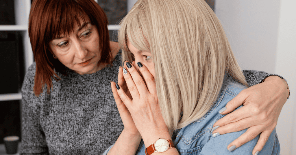 An older woman leans in to console a younger female, illustrating how easily she can offer comfort to those outside her closest circle.