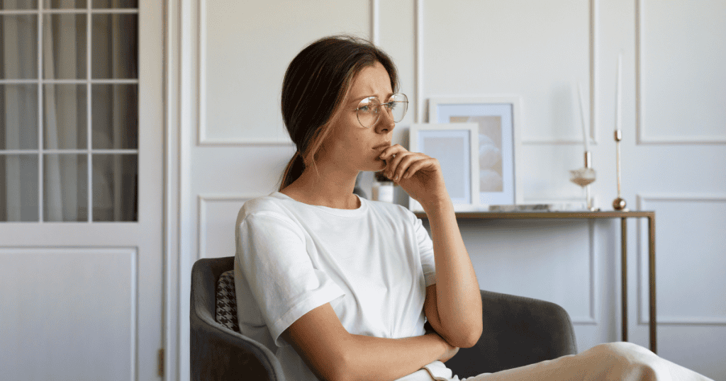 A woman with glasses rests her chin on her hand in deep thought, looking as though she is finally seeing a difficult situation with clarity.