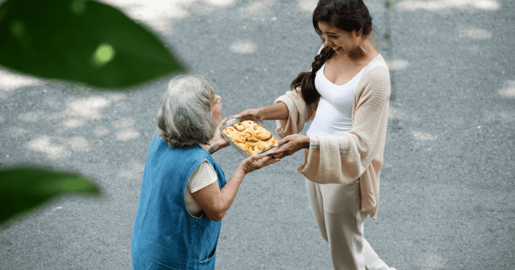 A young woman smiles warmly while offering a tray of baked goods to an elderly neighbor, a public display of generosity that masks a more complicated private reality.