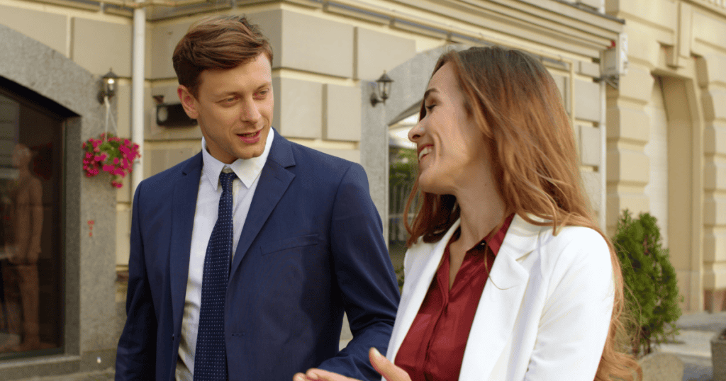 An impeccably dressed couple walks down a city street sharing a bright laugh, projecting a regal public image that stands in stark contrast to their personal dynamics.
