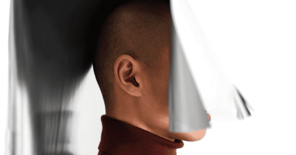 A profile view of a manโs head partially obscured by a heavy, metallic-colored shroud, representing the progressive loss of self during a dark transformation.